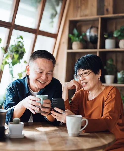 Couple looking at phone smiling drinking coffee
