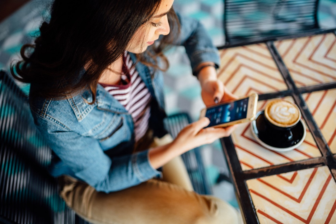 Young woman in a cafe reviewing investments on her phone.jpg