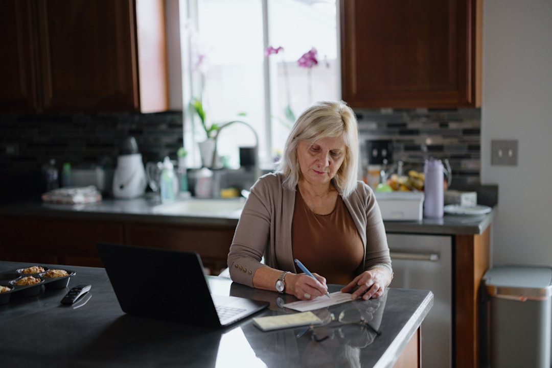 Female pension doing research in her kitchen using laptop and notepad.jpg