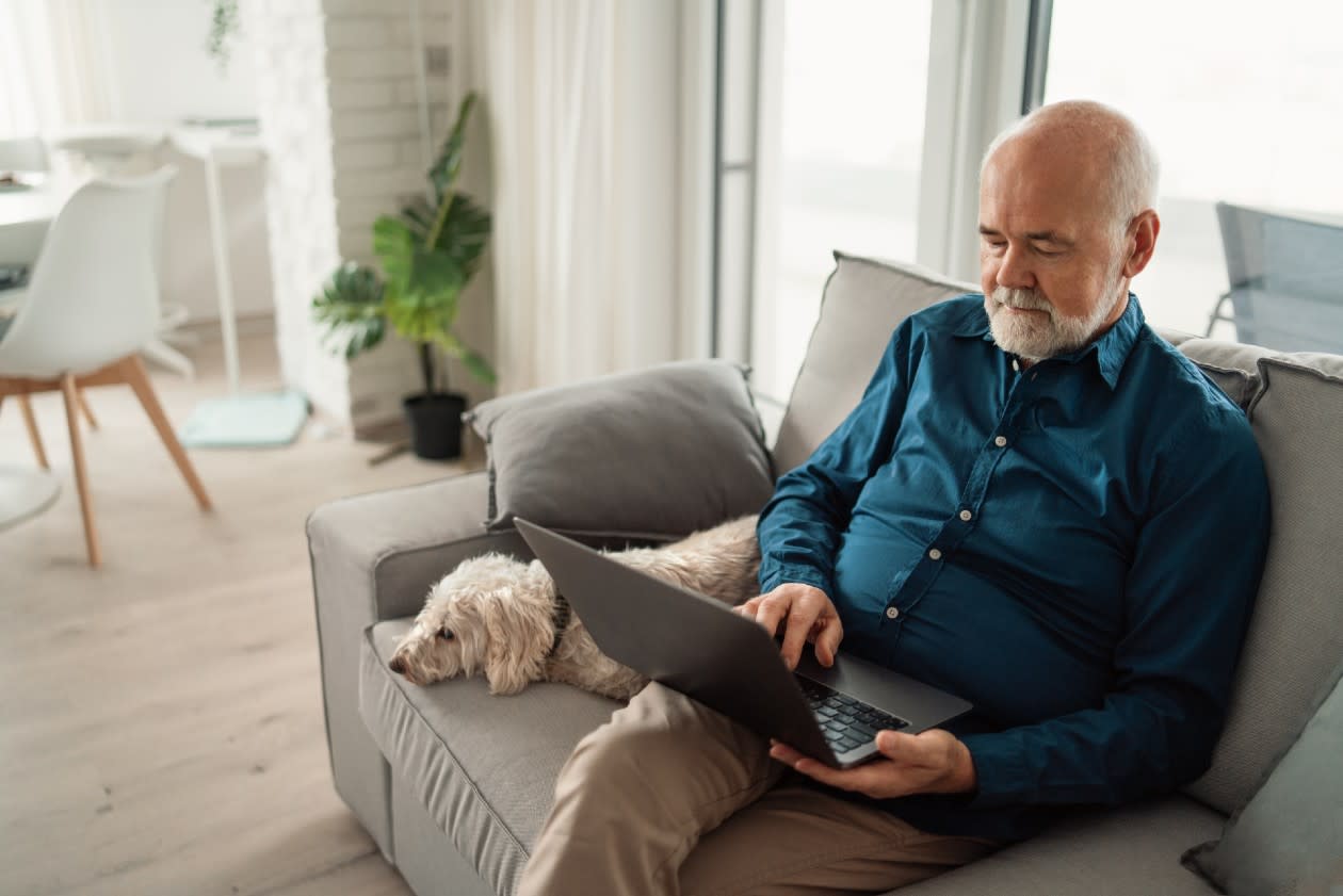 Retired man sat with dog on sofa reading laptop.jpg