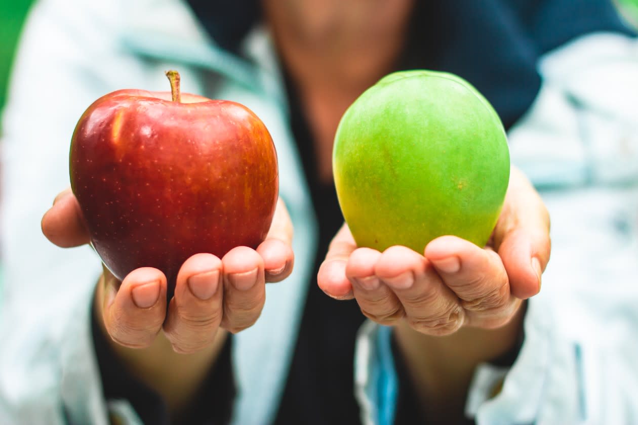 Woman holding out a green and red apple in each hand.jpg