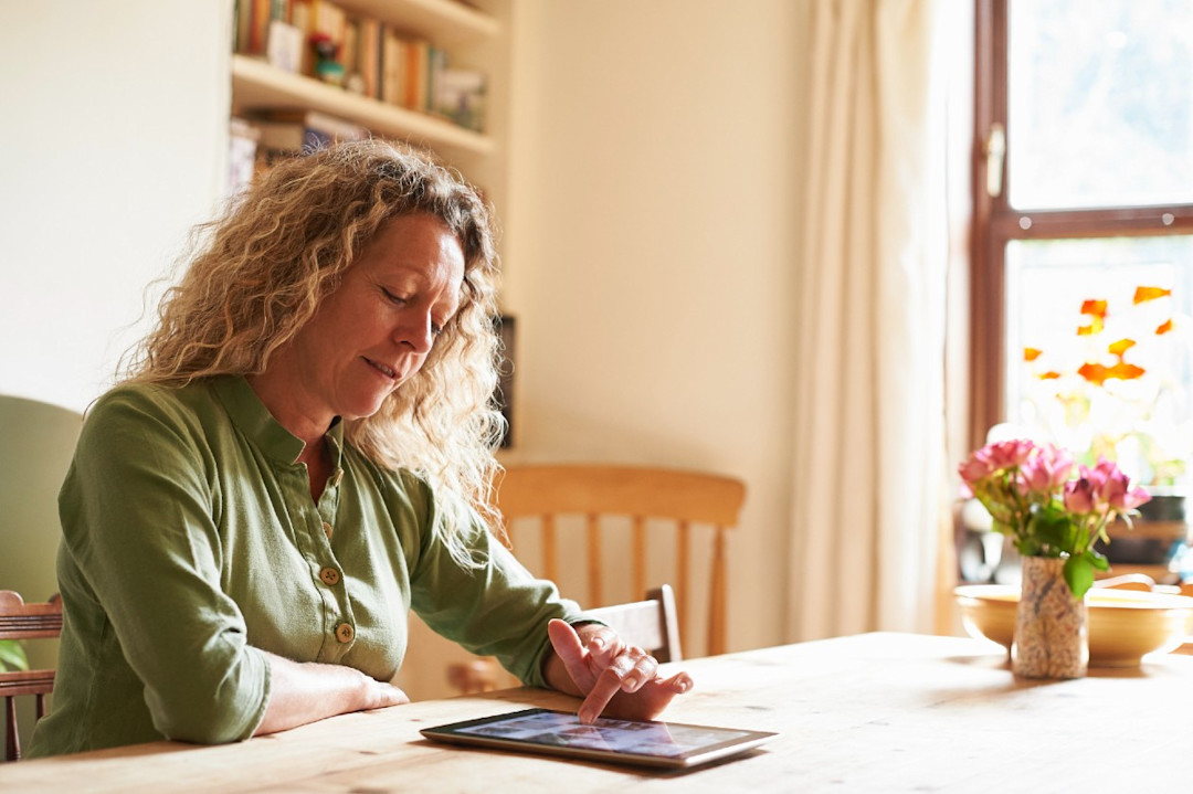 Woman doing research on her tablet in a sunny dining room
