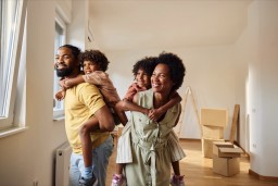 Happy black parents having fun while piggybacking their small kids after relocating into new apartment. 
