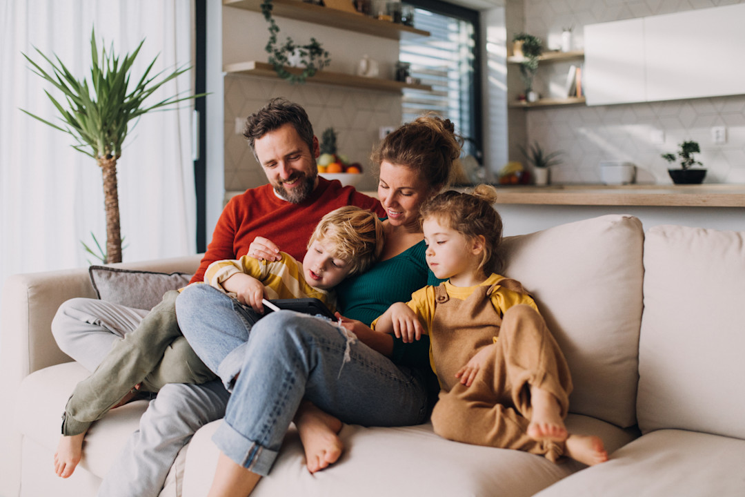 Little children bonding with parents on sofa at home and using tablet-GettyImages