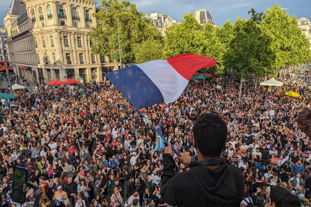 Man waving french flag in front of crowd in paris.png