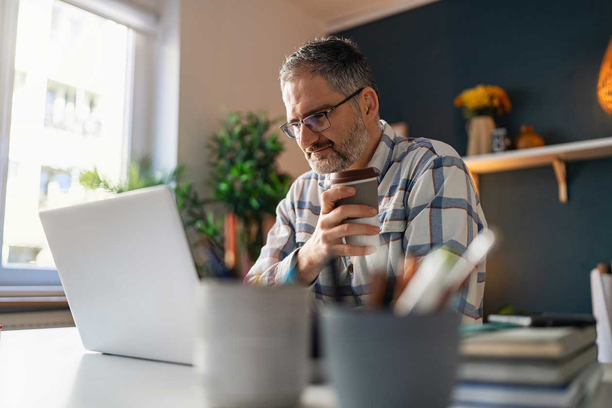 Older man reading information on laptop in the kitchen with a coffee.jpg