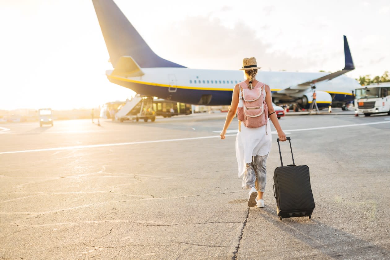 Woman walking to a plane on as sunny airport runway with suitcase.jpg