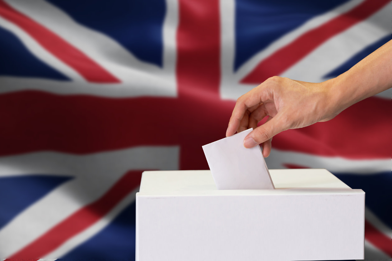 Close-up of man casting a vote with United Kingdom or UK flag blended in background- GettyImages