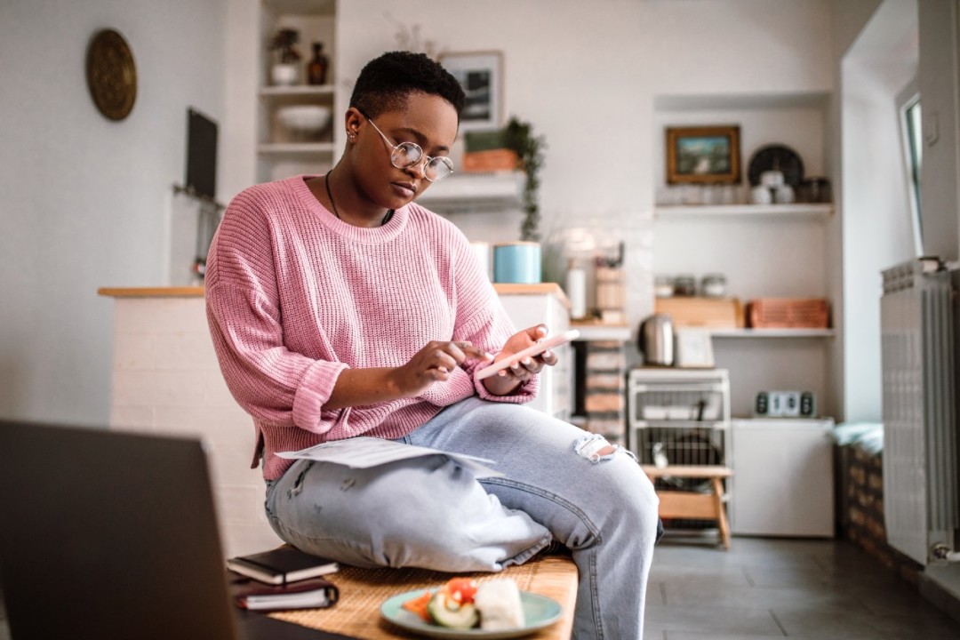 Woman in pink jumper sat on a chair in living area checking phone.jpg