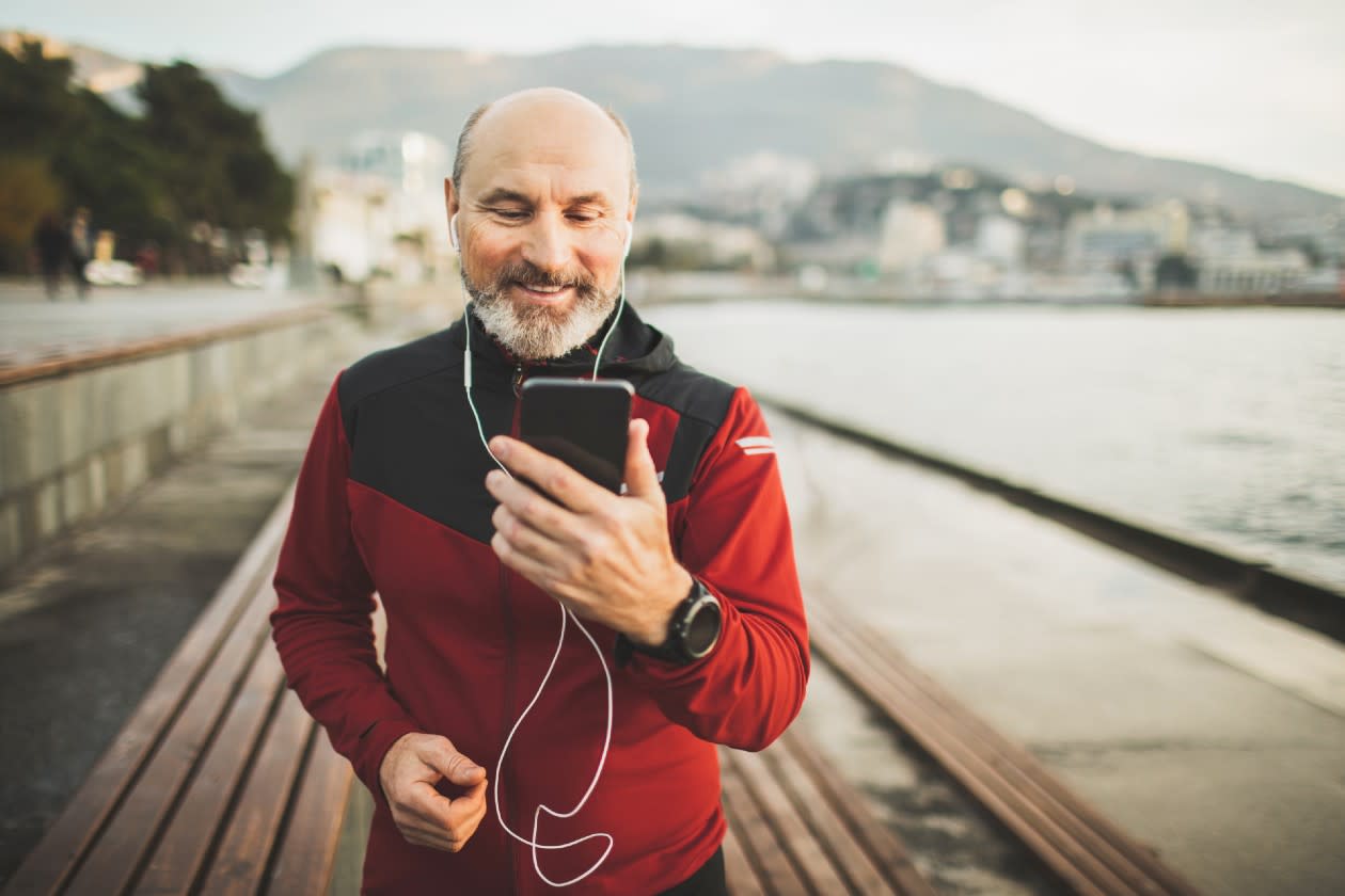 Pensioner out for a walk along a harbour while checking phone.jpg