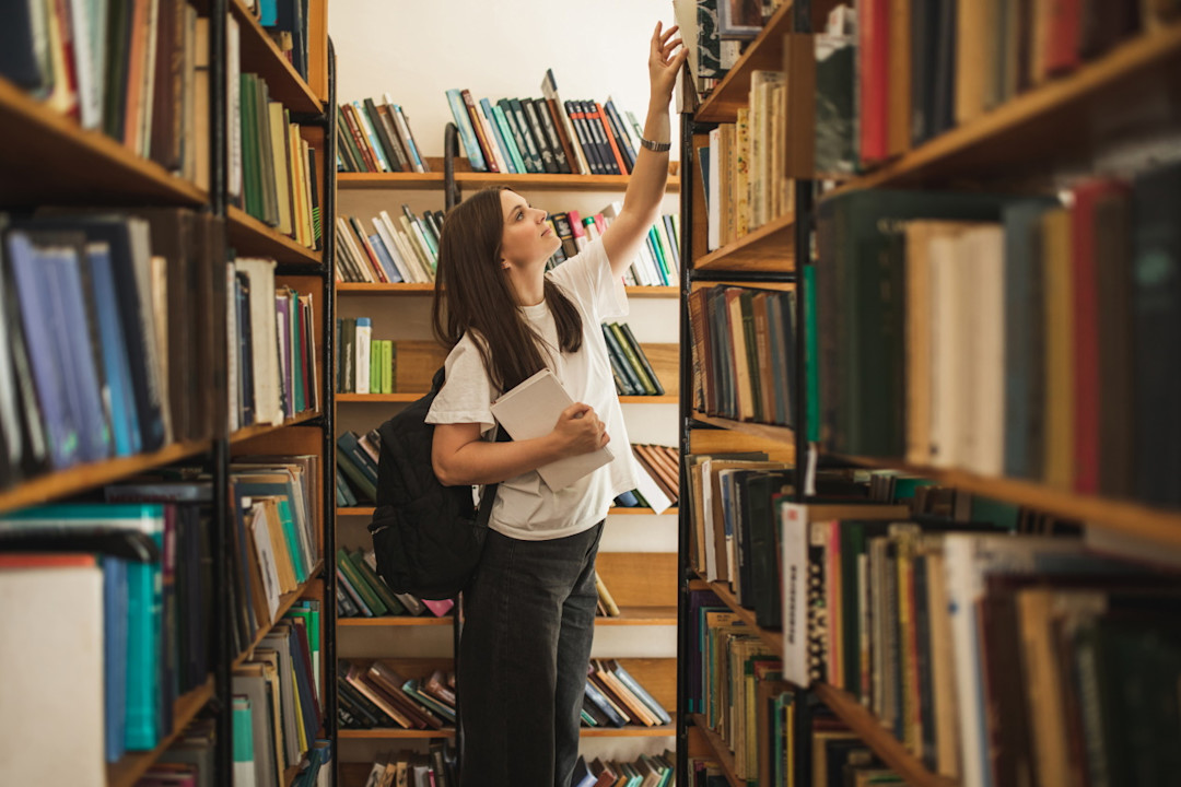 Female student reaching for a book in a library.jpg
