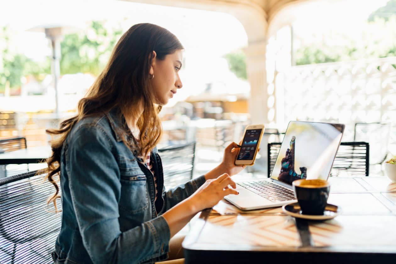 Young woman reviewing investments across her phone and laptop in a coffee shop.jpg