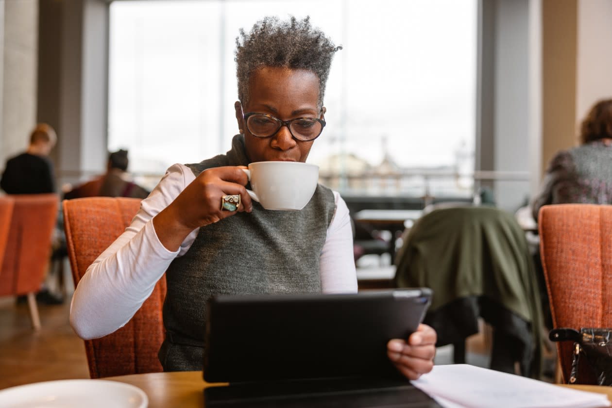 Pensioner sipping a coffee while reading news on a tablet device in a coffee shop.jpg