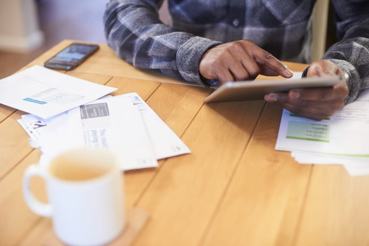 Male doing tax return on a tablet device at kitchen table surrounded by paperwork.jpg