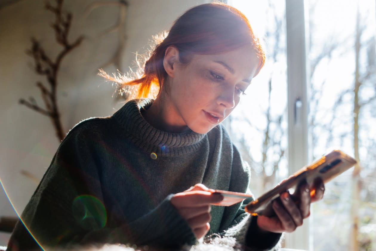 Young woman topping up her account on her phone in a sunny kitchen.jpg