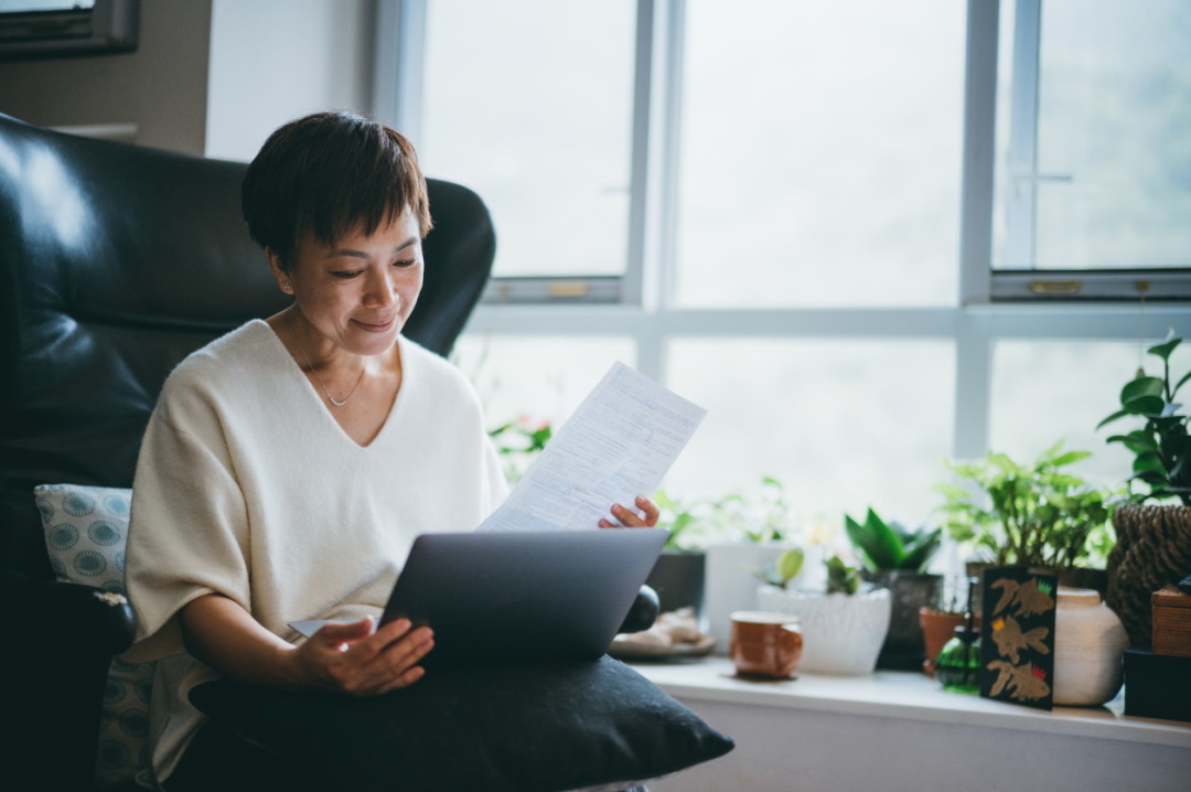 Woman smiling whilst checking her bank statements and bills.jpg