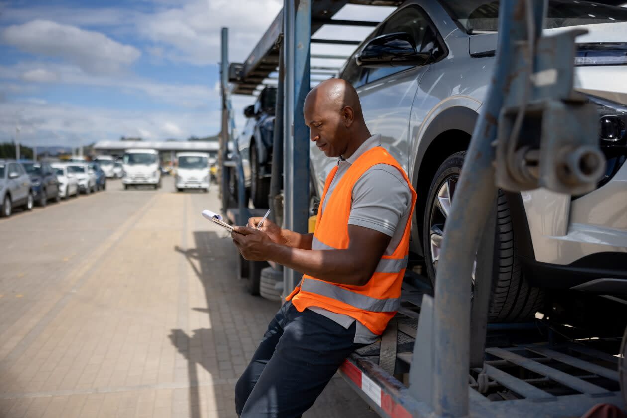 Man supervising the shipment of vehicles on a car transporter.jpg