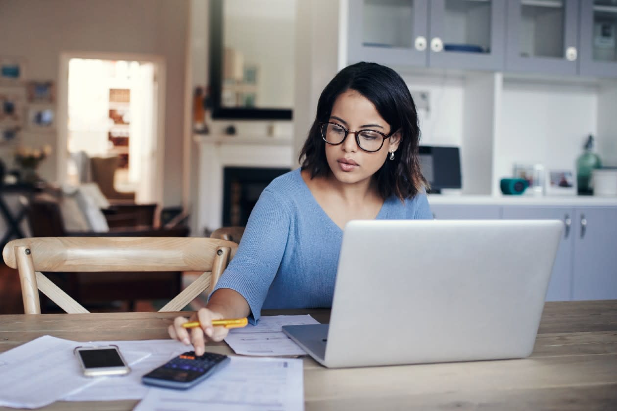Woman doing her finances at the kitchen table with paperwork phone and laptop.jpg