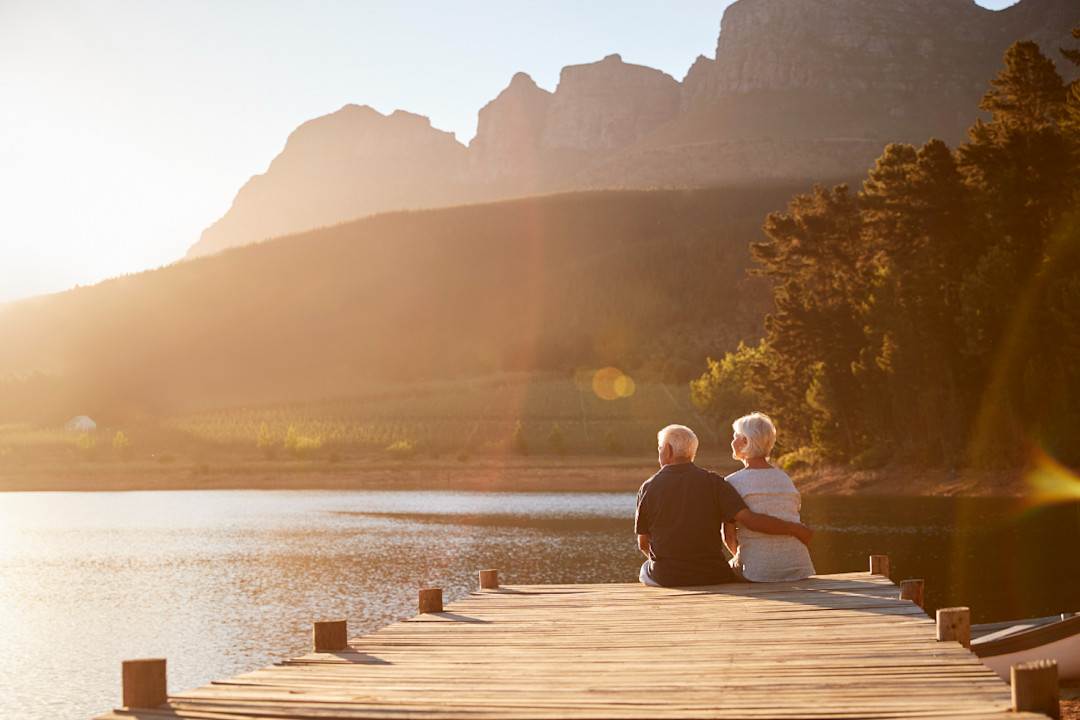 Romantic Senior Couple Sitting On Wooden Jetty By Lake.jpg