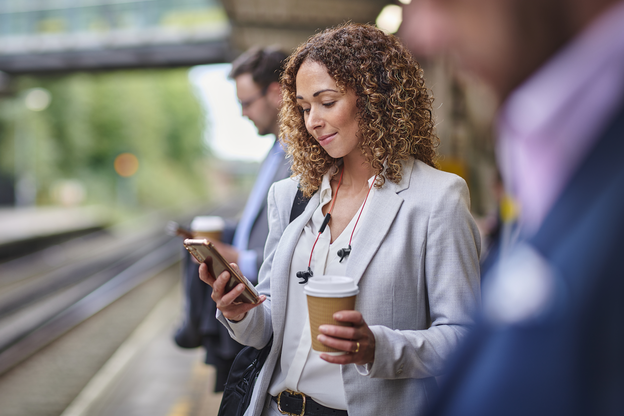 Woman reading the news on her phone on train platform.png