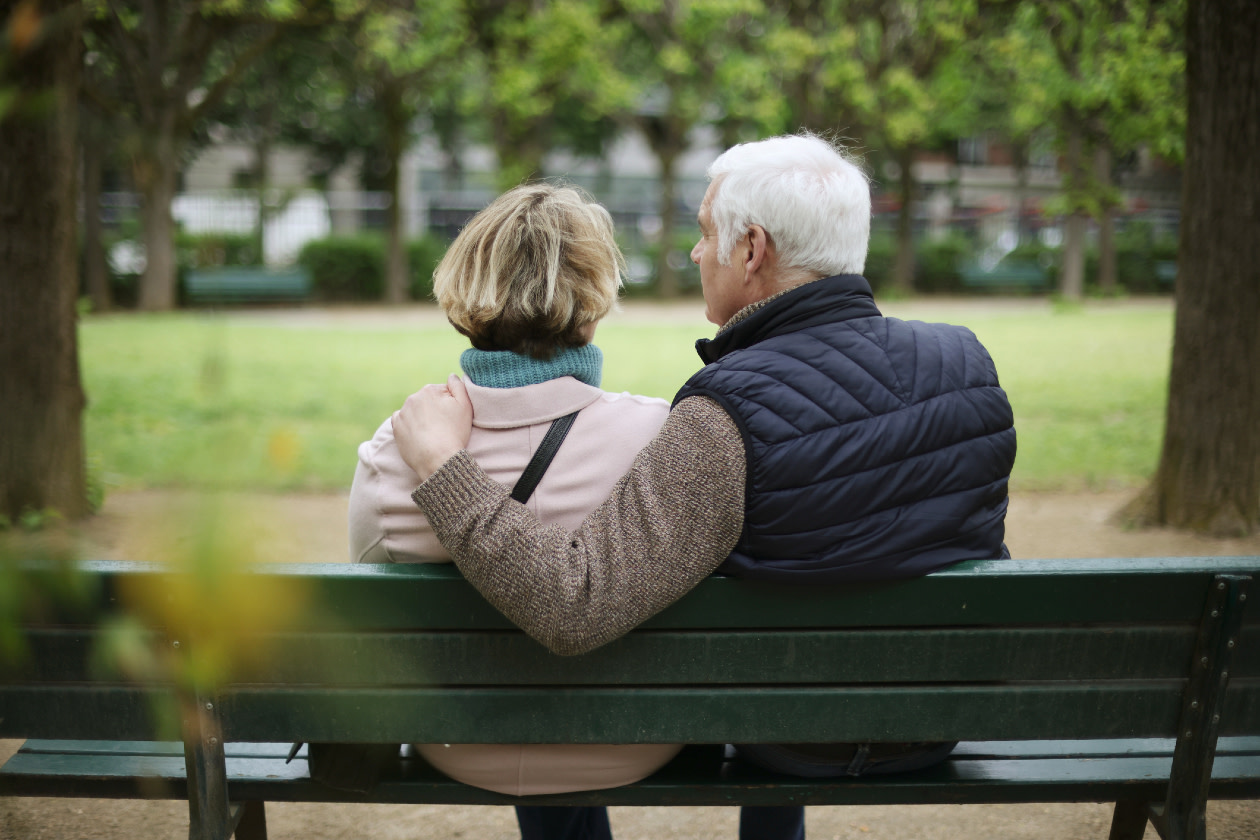 A senior couple embracing on a public bench in a park.jpg