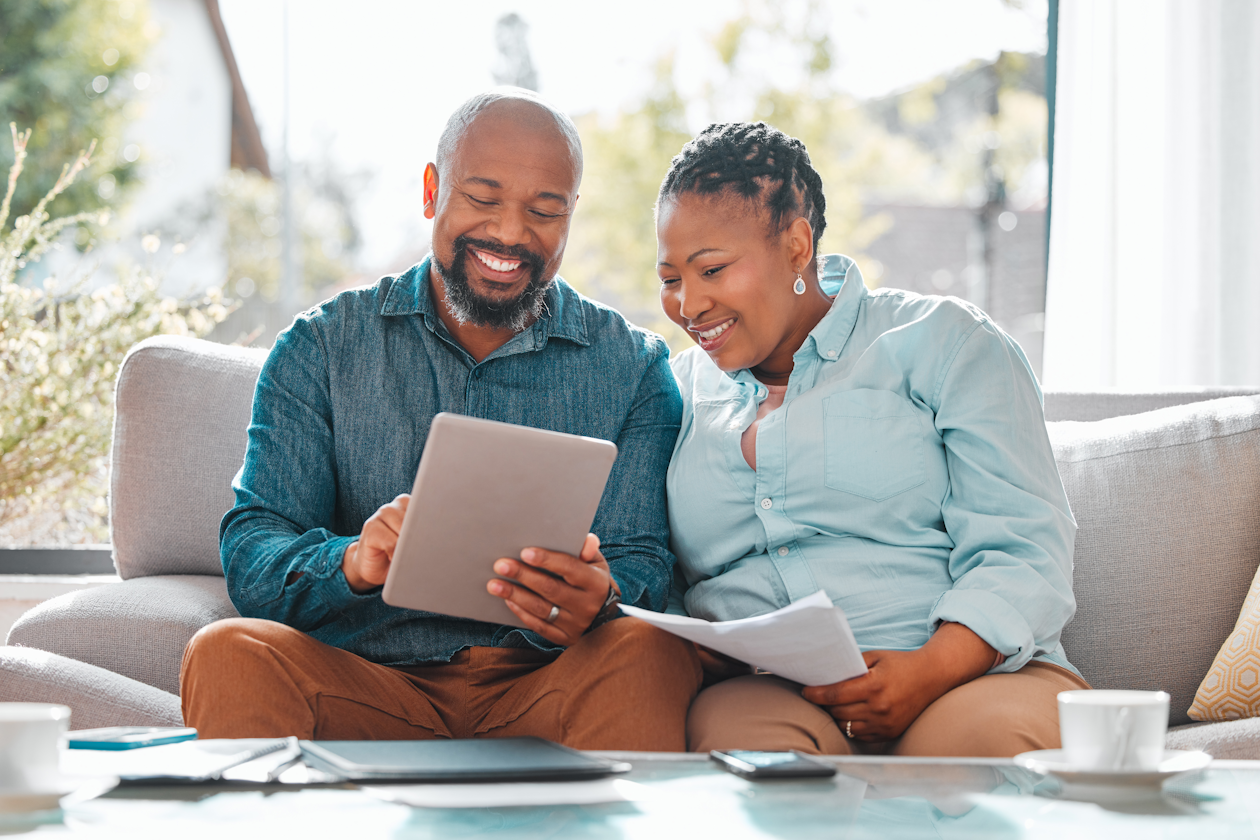 Couple smiling and looking at their investments on a tablet.png