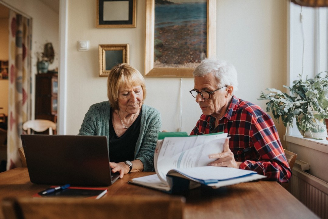 Pensioner couple reviewing finances using laptop and paperwork.jpg