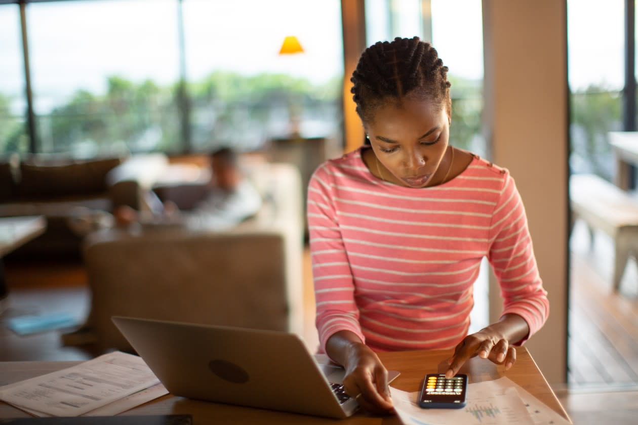 Young man doing her finances at kitchen table on laptop and notepad.jpg