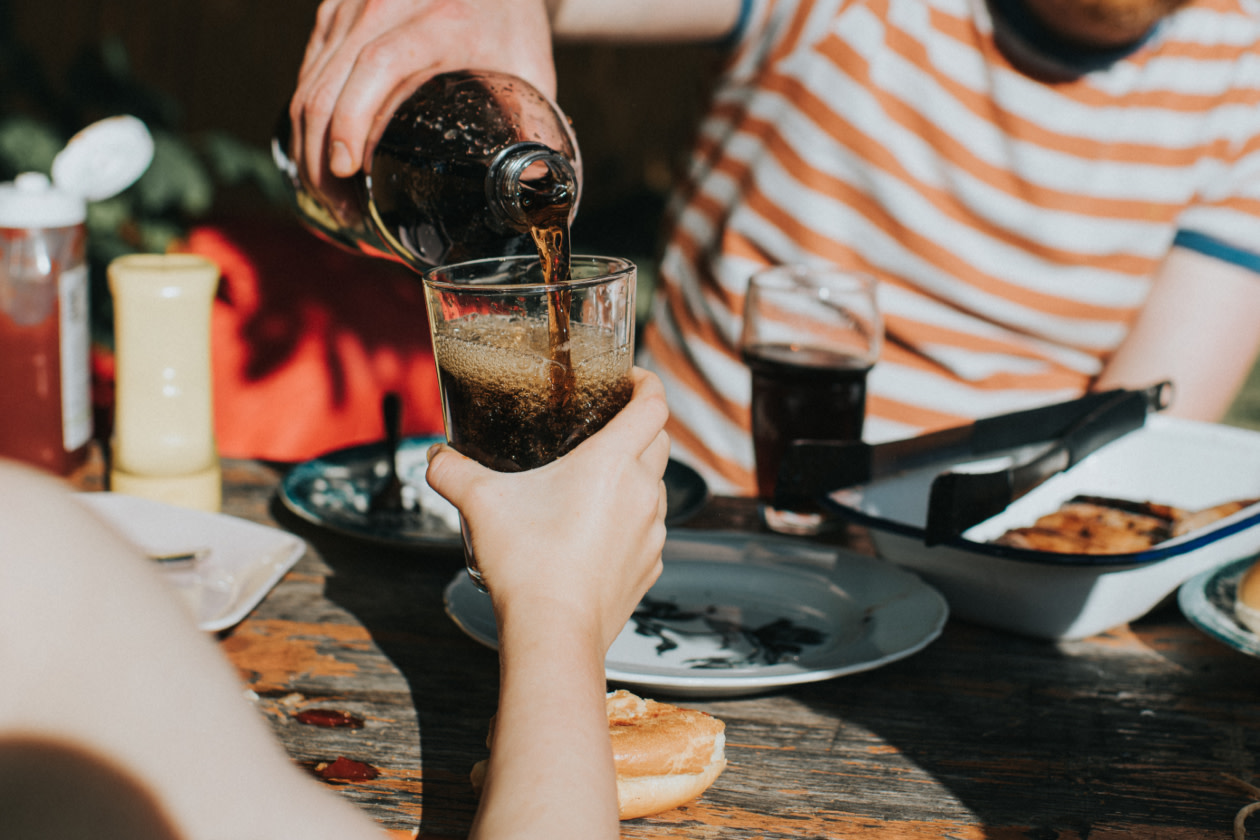 Child holds out a glass as a man pours a carbonated beverage into it - GettyImages