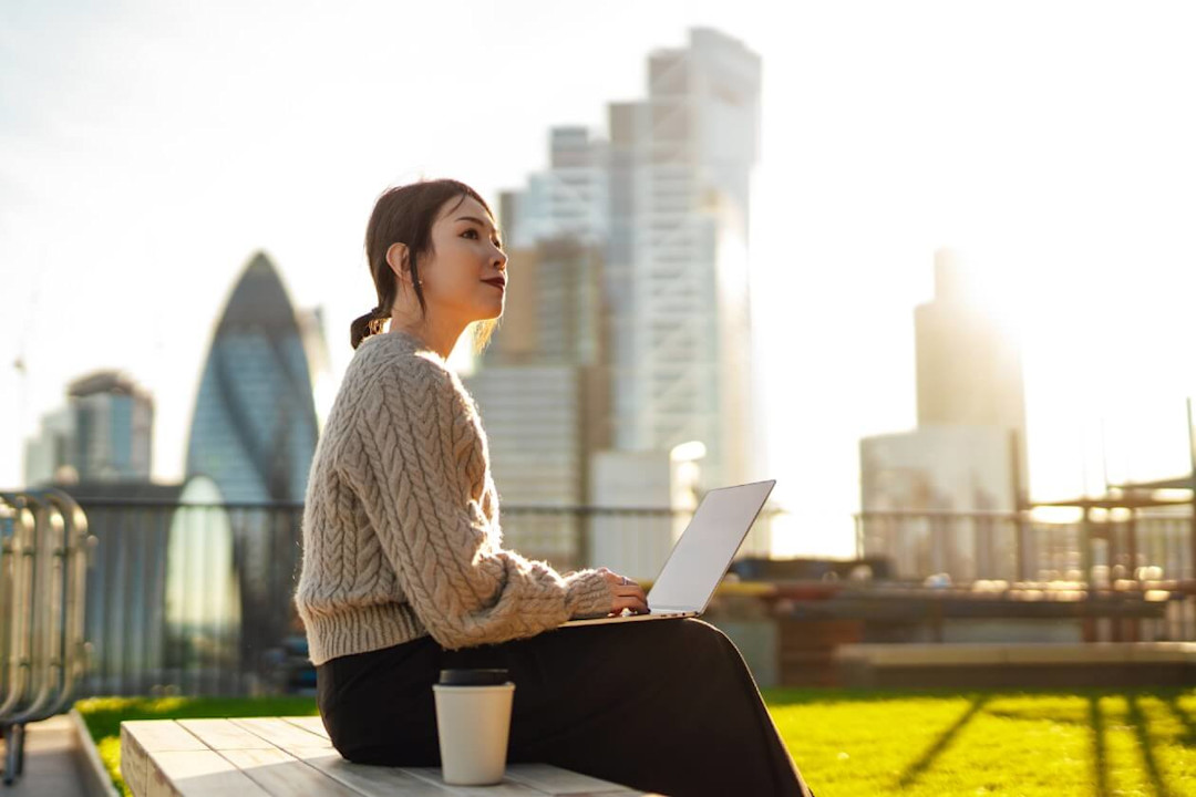 Young woman sat in front of london skyline on laptop