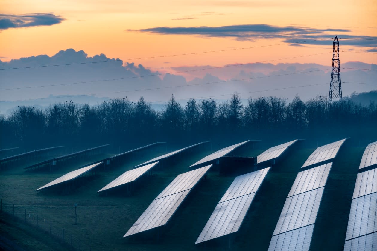 Solar energy park and conventional electricity pylon at sunset, Hampshire, England - GettyImages