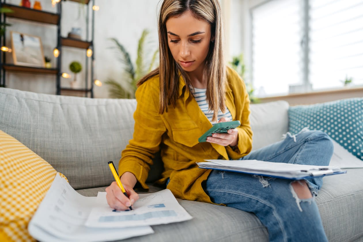 Woman doing her finances on the sofa using smartphone and paperwork.jpg