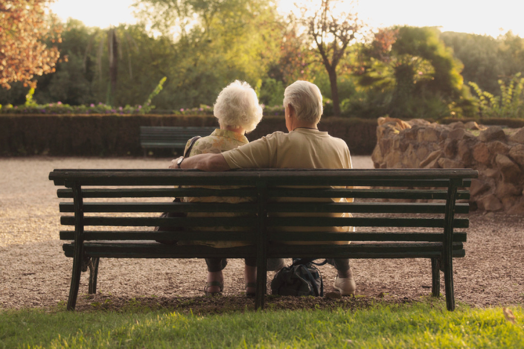 Senior couple sitting on bench in park, rear view- GettyImages