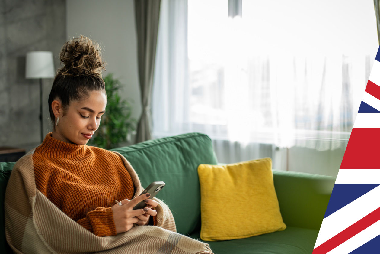 Woman in orange jumper sitting on sofa checking phone - Union jack overlay